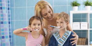 two kids brushing their teeth while their mom watches